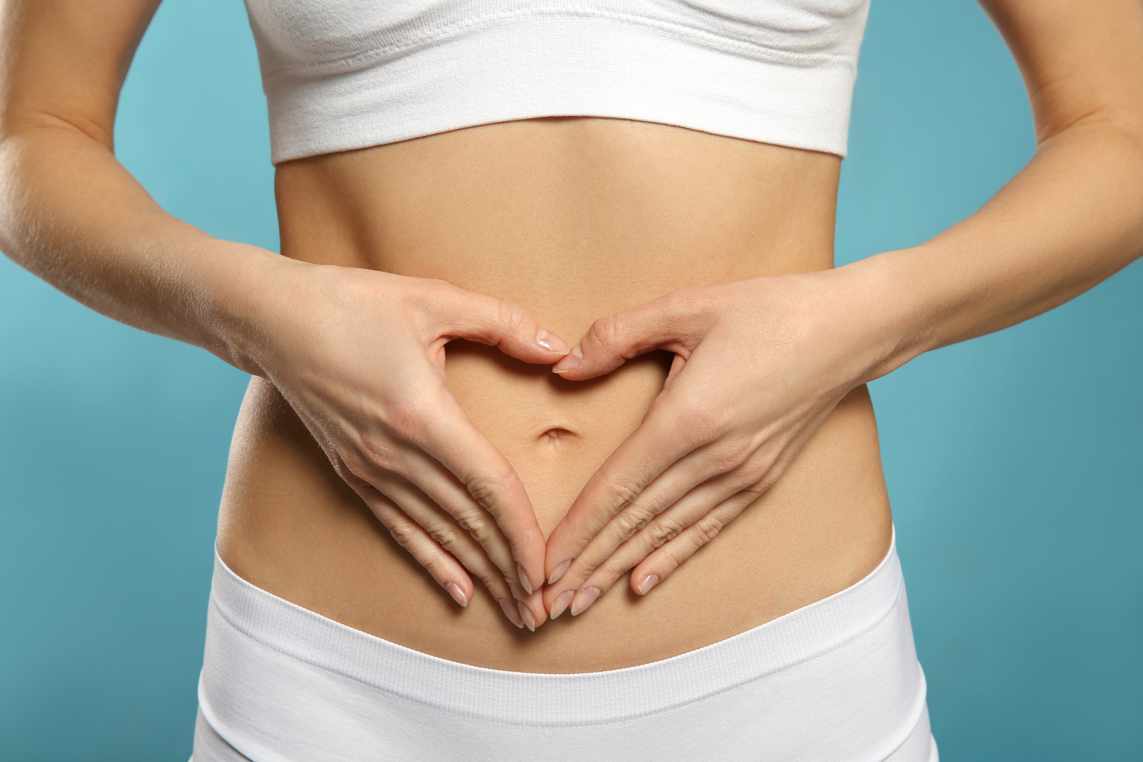 Woman Making Heart with Her Hands on Belly against Light Blue Background, Closeup